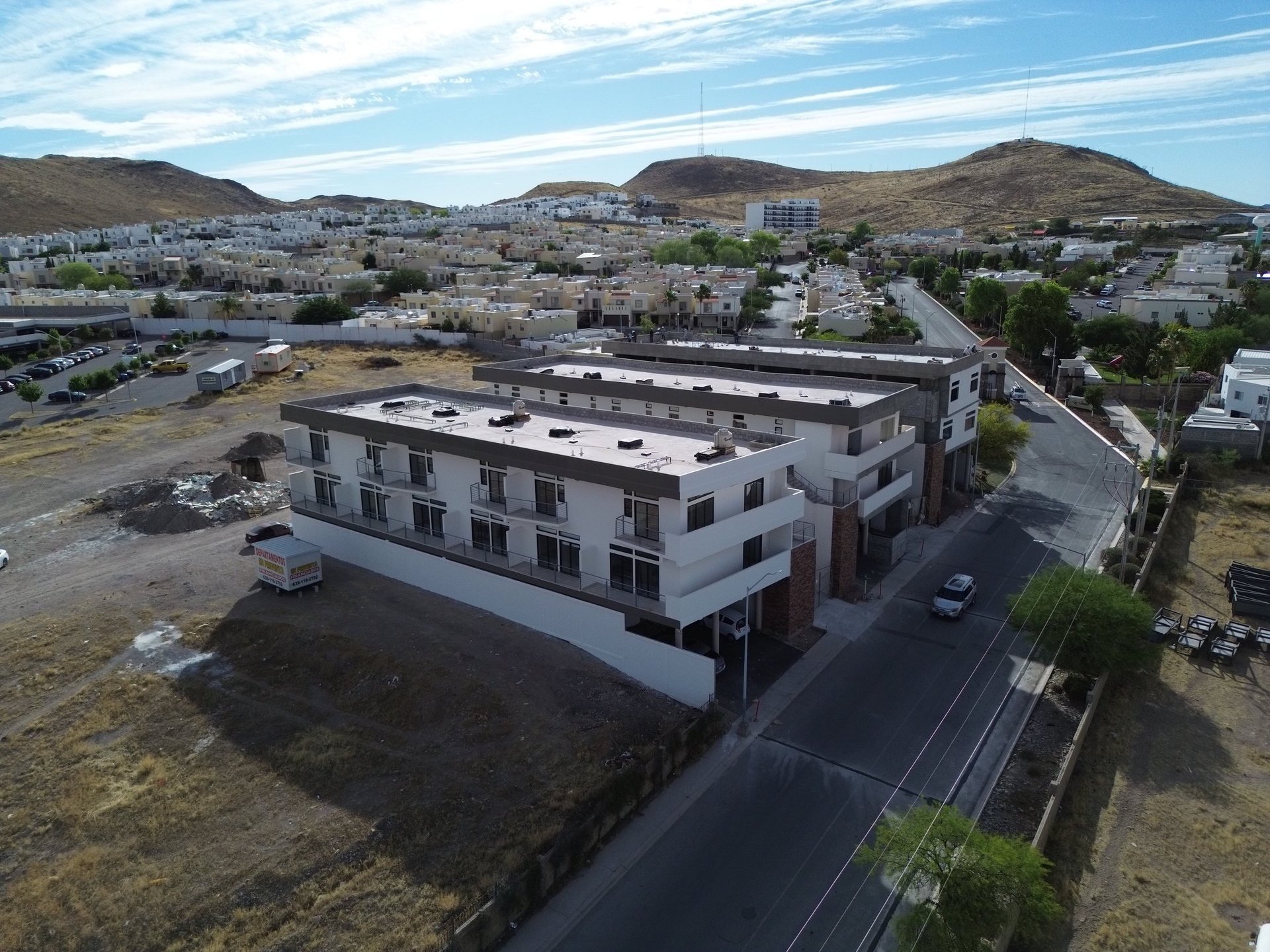 Aerial view of a modern white multi-story residential building with surrounding terrain and mountains in background