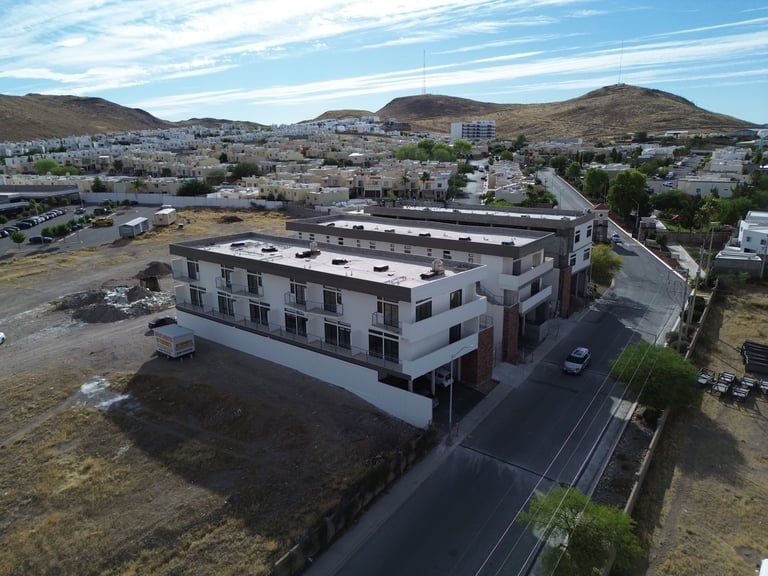 Aerial view of a modern white multi-story residential building with surrounding terrain and mountains in background