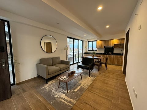 Sala de estar moderna en Alvatore con sofá gris, mesa de centro y cocina con gabinetes de madera