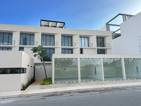 Modern white multi-story residential building with frosted glass fence and small courtyard under clear blue sky