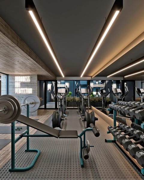 Modern gym interior with linear ceiling lights, exercise equipment including dumbbells and stationary bikes, and private workout pods