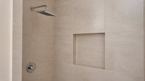 Modern bathroom shower with beige tile walls, chrome showerhead, valve, and built-in recessed niche