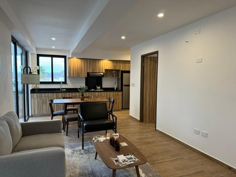 Departamento moderno de planta abierta en Alvatore: sala con sofá gris, comedor con sillas negras y cocina con gabinetes de madera