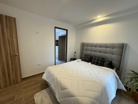 Recámara moderna Alvatore con cama tapizada en gris, ropa de cama blanca, piso de madera y decoración minimalista