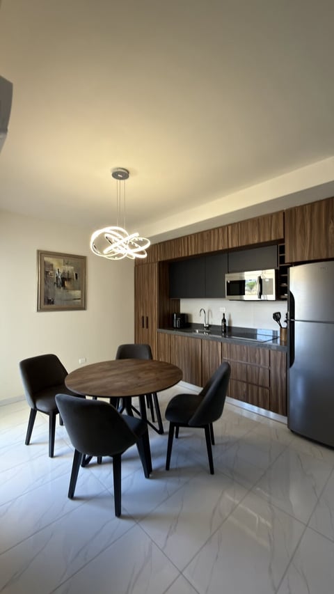 Cocina y comedor de London Cantera: cocina moderna con mesa redonda de madera, sillas negras, refrigerador de acero inoxidable y lámpara colgante contemporánea