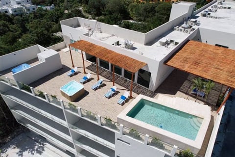 Aerial view of modern rooftop terrace with swimming pool, lounge chairs, wooden pergola, and white buildings