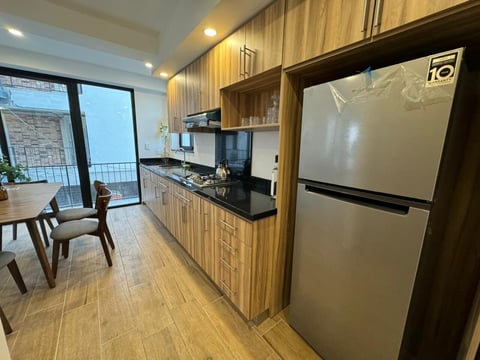 Cocina moderna Alvatore con gabinetes de madera, electrodomésticos de acero inoxidable, cubiertas negras y comedor con puertas de vidrio hacia el balcón