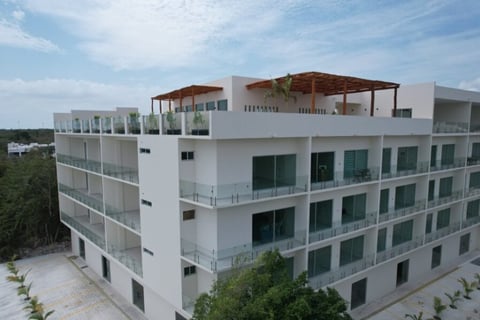 Modern white multi-story residential building with green-trimmed windows, balconies, and a rooftop terrace under blue sky