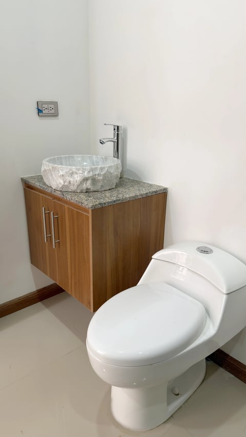Baño con inodoro blanco, mueble de madera con cubierta de mármol y lavabo de piedra circular con grifería