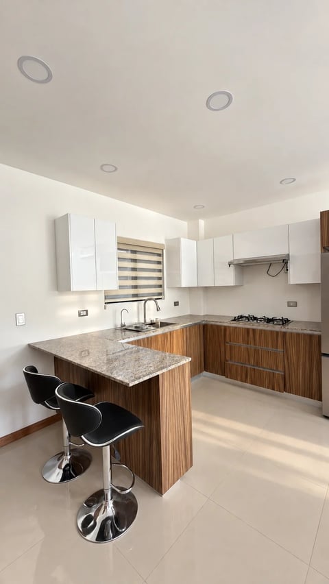 Cocina con alacena blanca, barra con acabado tipo madera, cubierta de granito y bancos negros