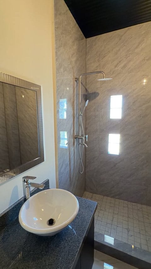 Baño de London Cantera: baño moderno con lavabo blanco redondo de sobreponer, cubierta oscura, espejo con marco y regadera con paredes de azulejo y cabezal de lluvia superior