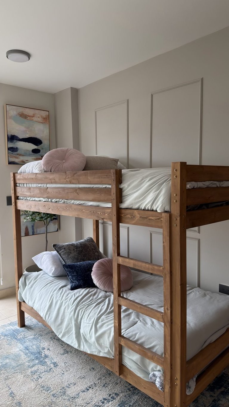 Wooden bunk bed with white bedding and decorative pillows in a modern bedroom with beige walls and framed artwork