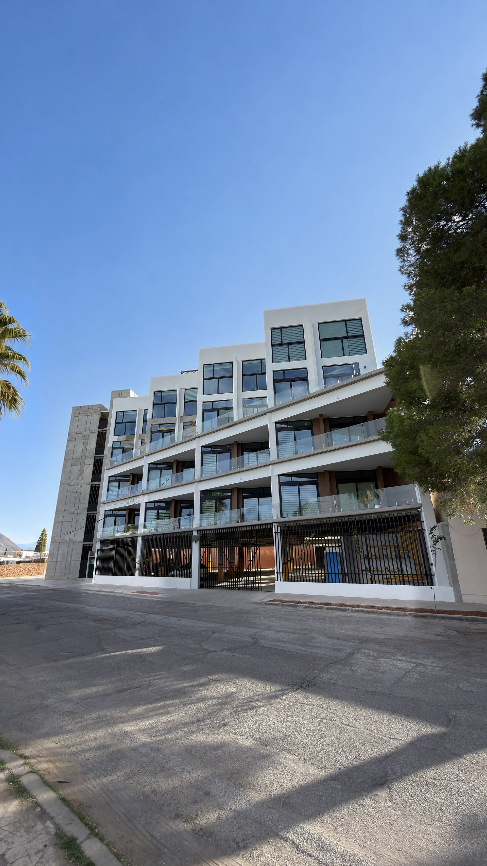 Fachada del edificio residencial Torre Alteza con balcones horizontales y malla metálica bajo cielo despejado
