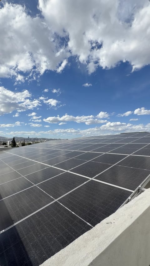 Paneles solares en azotea bajo cielo azul con nubes y vista lejana de la ciudad