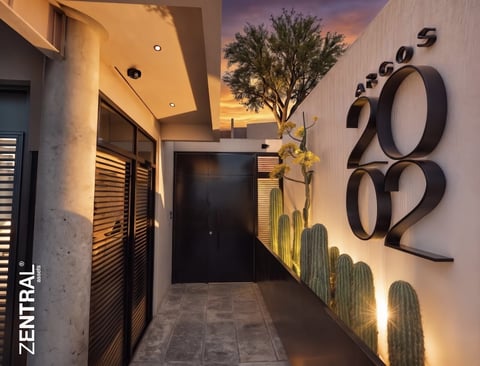 Modern hallway entrance with house number 2002, cactus wall mural, decorative tree, and sunset sky ceiling at dusk