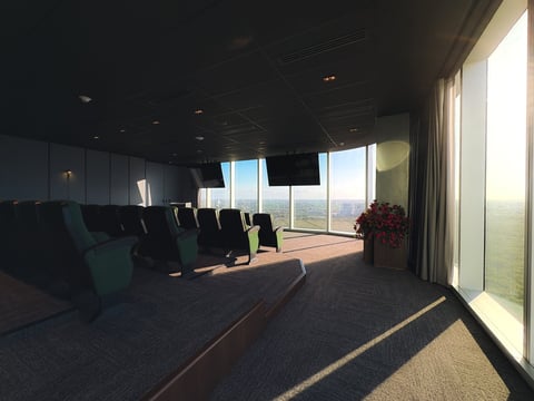 Auditorio de The Sky con filas de sillas, ventanales de piso a techo con vista a la ciudad y luz natural