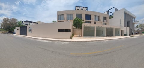 Modern multi-story residential building with beige facade on a street corner, featuring large windows and green planters