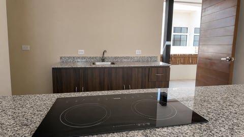 Built-in electric cooktop in a modern kitchen with granite countertop, dark cabinetry, and backsplash