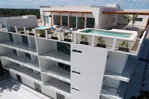 Aerial view of a modern white residential building with rooftop pool, terraces, and green plants under clear sky